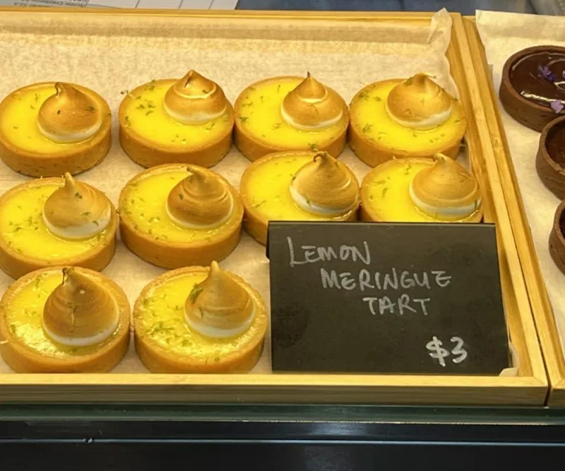 Slate price cards chalked by hand in the cat in the hat display case, beside a tray of lemon meringue tarts