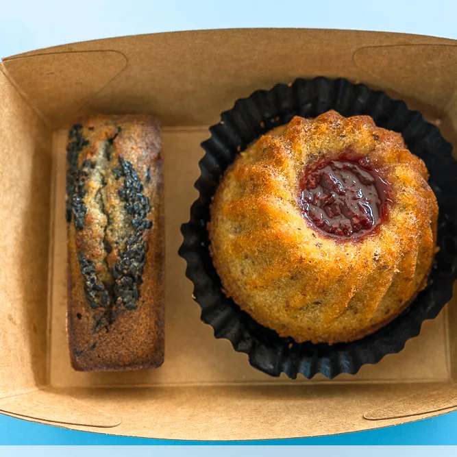 Black sesame financier from cat in the hat, in a kraft box beside a raspberry-filled bundt cake